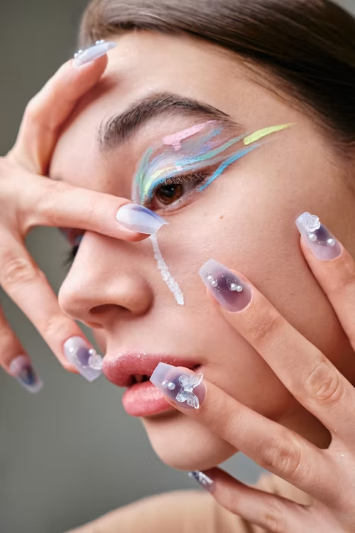 A close-up of a model featuring artistic pastel graphic eyeliner and matching 3D butterfly nail art. A close-up of a model featuring artistic pastel graphic eyeliner and matching 3D butterfly nail art.